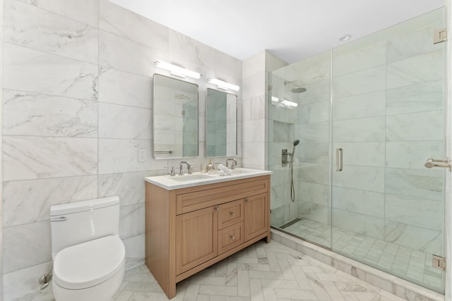 bathroom with tile walls, double vanity, toilet, a stall shower, and a sink