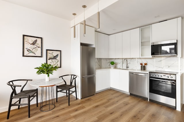 kitchen featuring decorative backsplash, pendant lighting, white cabinets, and stainless steel appliances