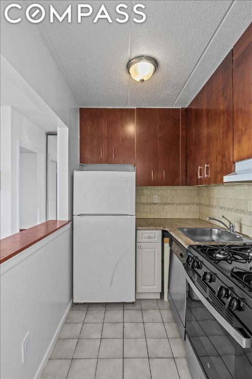 kitchen with sink, light tile patterned floors, gas range oven, stainless steel dishwasher, and white fridge