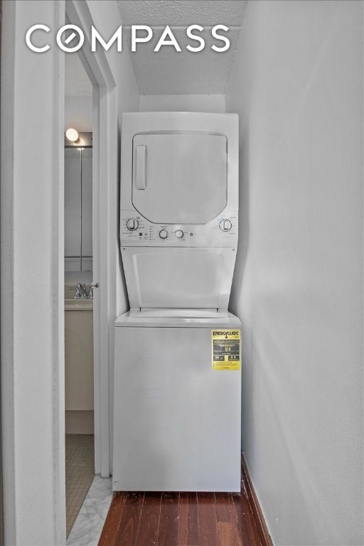 clothes washing area with stacked washer and dryer, dark hardwood / wood-style flooring, and sink