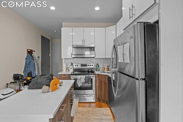 kitchen with light stone countertops, white cabinets, stainless steel appliances, light hardwood / wood-style floors, and backsplash