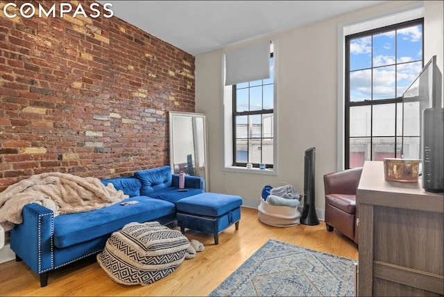 living room with wood-type flooring, plenty of natural light, and brick wall