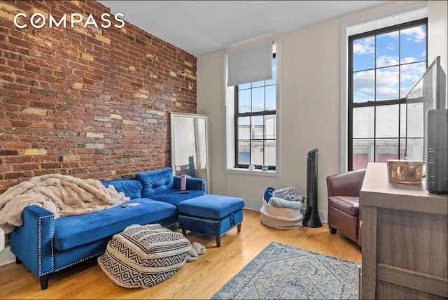 living area with brick wall, wood finished floors, and a healthy amount of sunlight