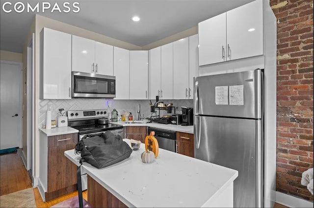 kitchen featuring tasteful backsplash, sink, white cabinetry, light wood-type flooring, and appliances with stainless steel finishes