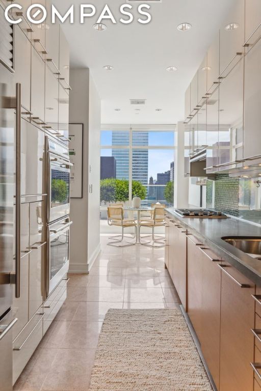 kitchen with appliances with stainless steel finishes, sink, backsplash, light tile patterned floors, and floor to ceiling windows