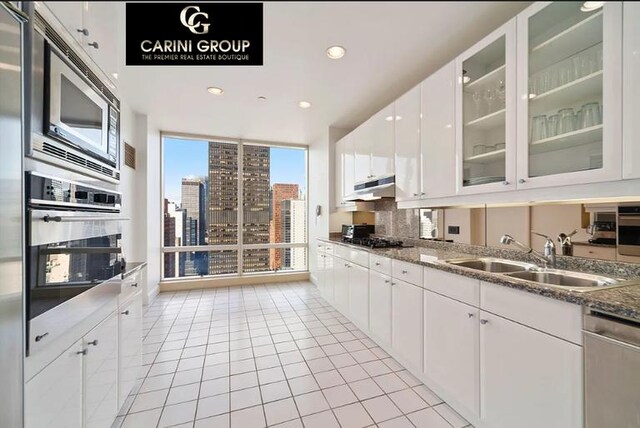 845 United Nations Plz Unit 36C, New York City, NY 10017 - kitchen featuring a sink, appliances with stainless steel finishes, light tile patterned flooring, a view of city, and glass insert cabinets
