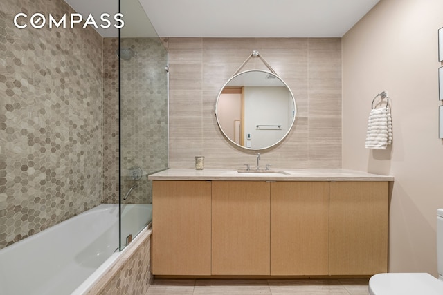 full bath with toilet, tile walls, vanity, and tiled shower / bath combo