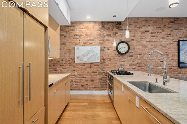 kitchen with pendant lighting, brick wall, light hardwood / wood-style floors, sink, and light stone counters