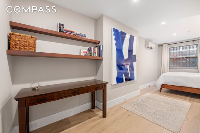 bedroom with wood finished floors, a wall unit AC, recessed lighting, and baseboards