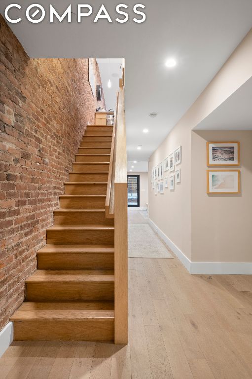 stairs featuring brick wall and hardwood / wood-style flooring