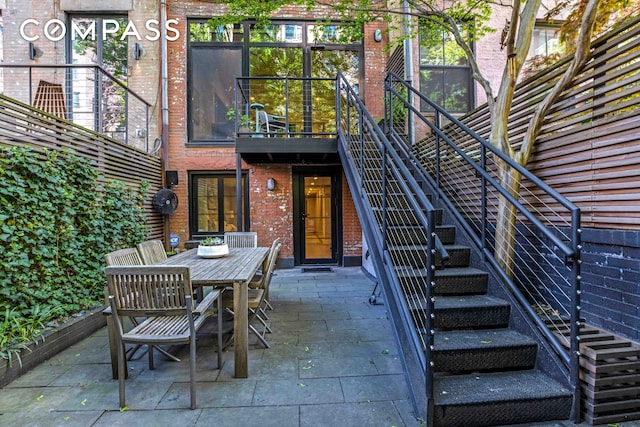 rear view of property with stairs, brick siding, a patio, and outdoor dining space