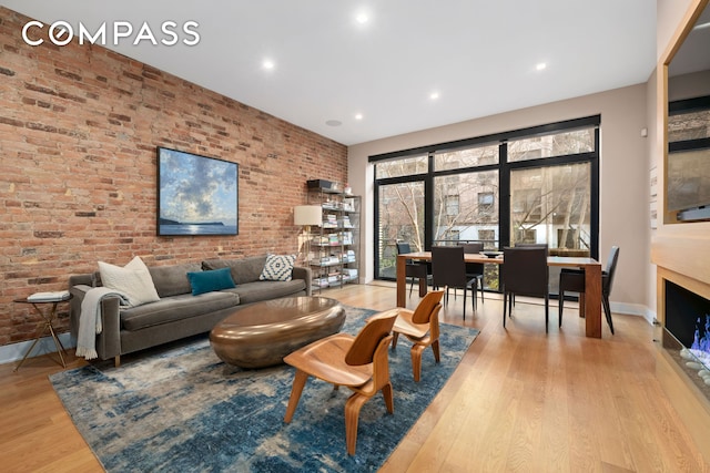 living room featuring light wood-style floors, recessed lighting, baseboards, and brick wall