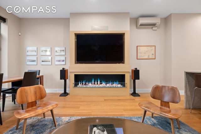 living room featuring a fireplace, wood finished floors, an AC wall unit, and baseboards