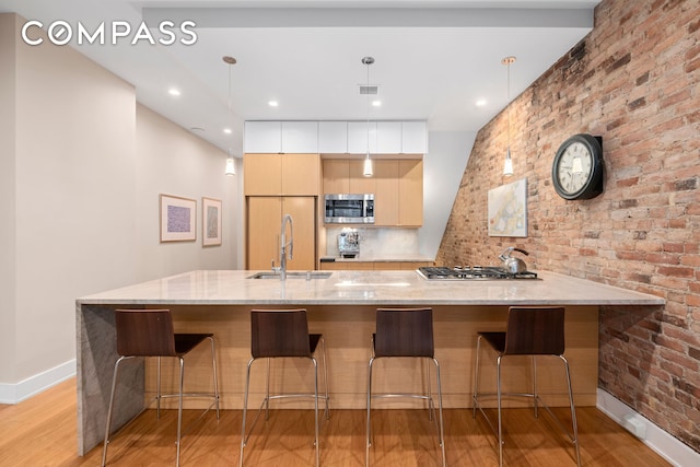 kitchen with stainless steel appliances, a sink, light wood-type flooring, baseboards, and a breakfast bar
