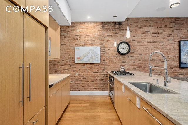 kitchen with light stone counters, light wood finished floors, hanging light fixtures, a sink, and brick wall