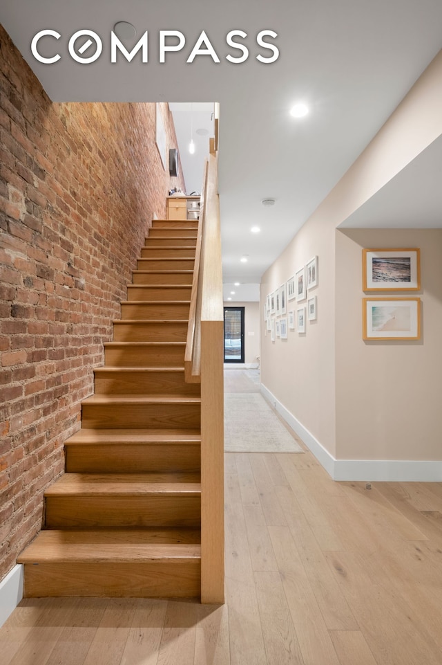 stairway featuring brick wall, baseboards, hardwood / wood-style floors, and recessed lighting