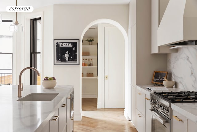 kitchen with stainless steel range with gas cooktop, tasteful backsplash, a sink, light stone countertops, and premium range hood