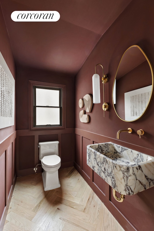 half bath featuring a wainscoted wall, lofted ceiling, toilet, and a decorative wall