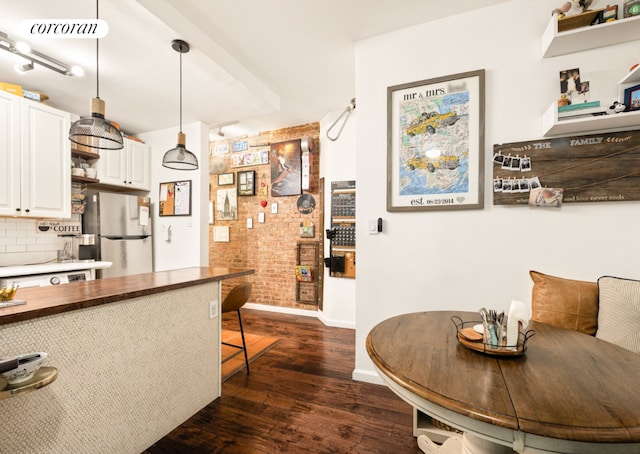 kitchen with white cabinets, dark wood-type flooring, backsplash, hanging light fixtures, and stainless steel refrigerator