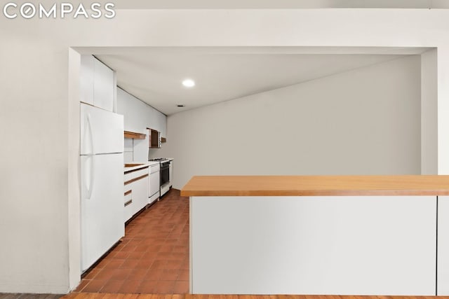 kitchen featuring gas range oven, white cabinetry, and white fridge