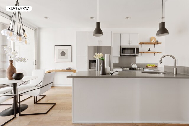 kitchen with stainless steel appliances, white cabinetry, sink, and decorative light fixtures