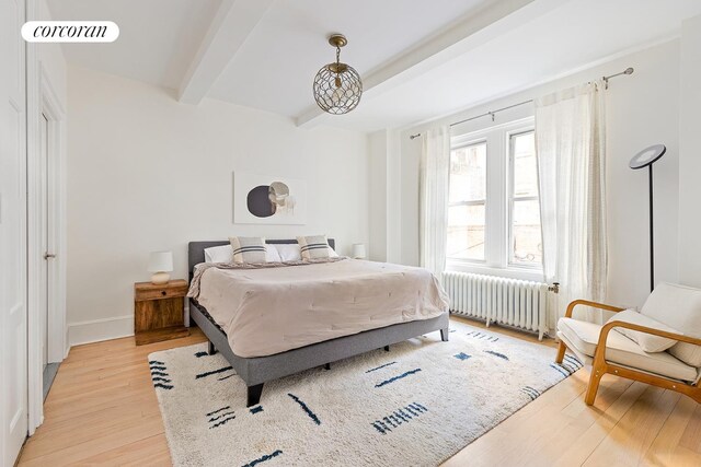 bedroom with beam ceiling, radiator heating unit, and light hardwood / wood-style floors