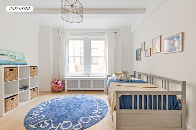 bedroom featuring beamed ceiling, radiator, and hardwood / wood-style floors