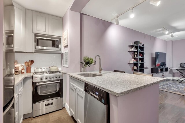 kitchen with rail lighting, kitchen peninsula, stainless steel appliances, tasteful backsplash, and sink