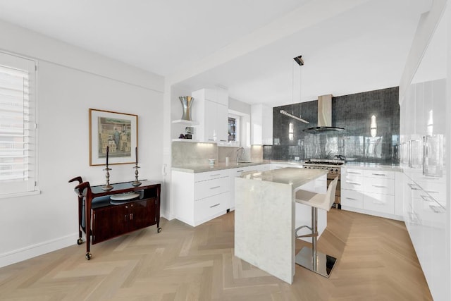 kitchen with white cabinets, stainless steel range, a kitchen island, and wall chimney range hood