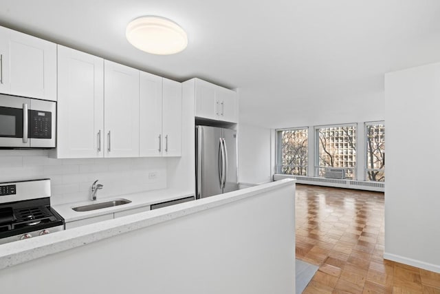 kitchen with sink, light parquet floors, stainless steel appliances, light stone counters, and white cabinets