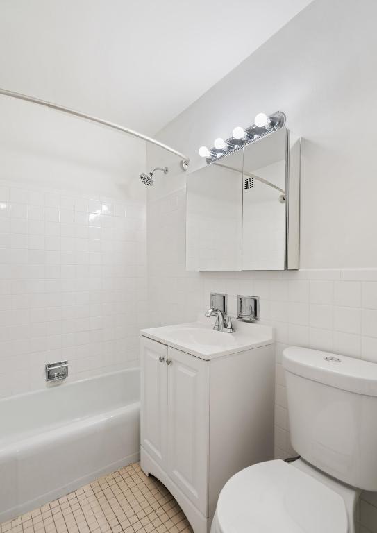 full bathroom featuring tile walls, tiled shower / bath combo, vanity, tile patterned floors, and toilet