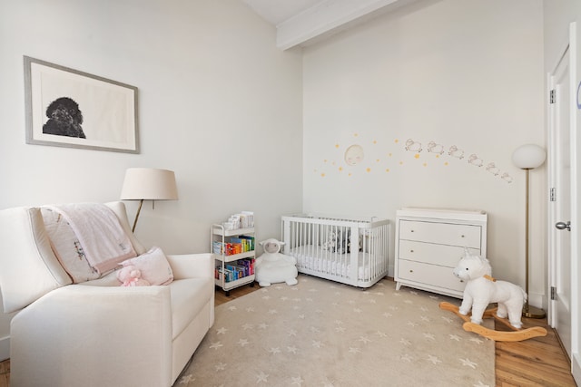 bedroom with light hardwood / wood-style floors, beamed ceiling, and a crib