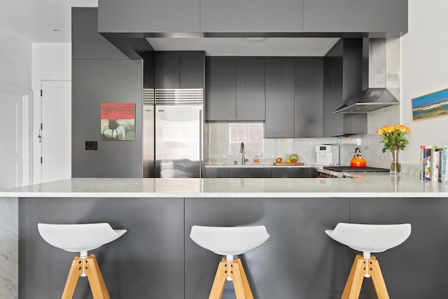 kitchen with stainless steel appliances, tasteful backsplash, kitchen peninsula, and wall chimney exhaust hood