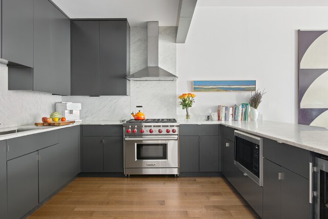 kitchen featuring gray cabinets, appliances with stainless steel finishes, hardwood / wood-style floors, backsplash, and wall chimney exhaust hood