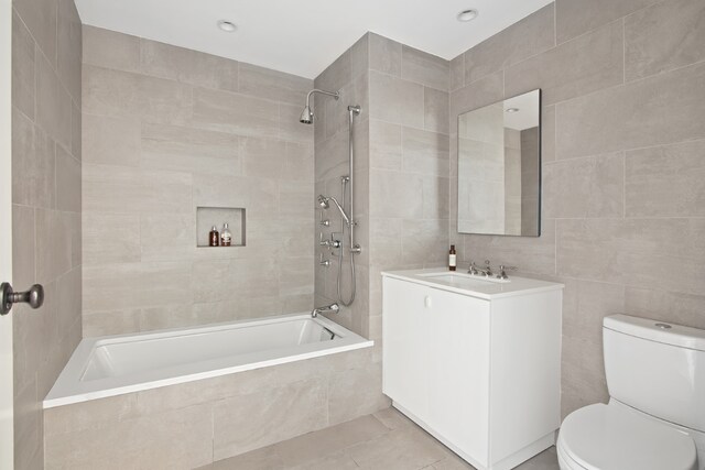 full bathroom with tile patterned floors, toilet, tiled shower / bath, tile walls, and vanity