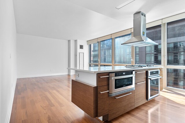 kitchen with light hardwood / wood-style floors, appliances with stainless steel finishes, a wall of windows, and range hood