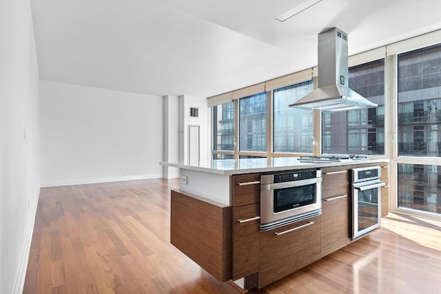 kitchen with light hardwood / wood-style flooring, exhaust hood, a wall of windows, and appliances with stainless steel finishes