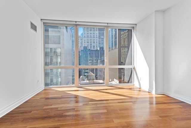 unfurnished room with visible vents, wood finished floors, baseboards, and expansive windows