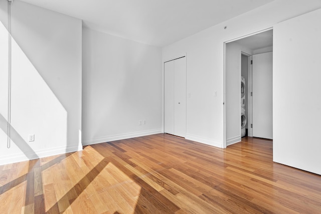 empty room with baseboards, light wood-style floors, and stacked washer and clothes dryer