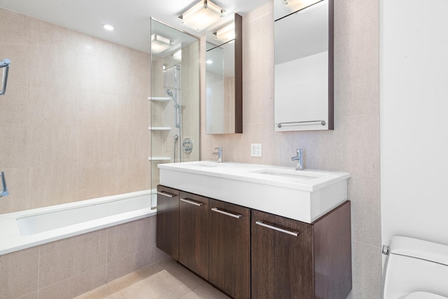 full bathroom featuring toilet, double vanity, tiled shower / bath combo, tile patterned floors, and a sink