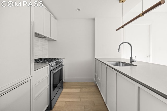 kitchen with gas stove, white cabinetry, tasteful backsplash, sink, and light wood-type flooring