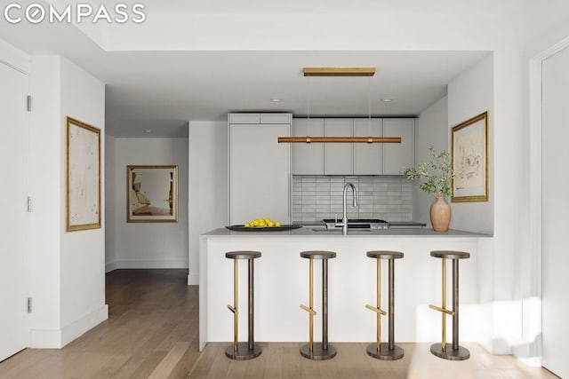 kitchen with white cabinets, tasteful backsplash, light hardwood / wood-style floors, sink, and kitchen peninsula