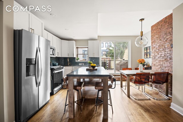 kitchen with white cabinets, appliances with stainless steel finishes, decorative backsplash, hanging light fixtures, and hardwood / wood-style flooring