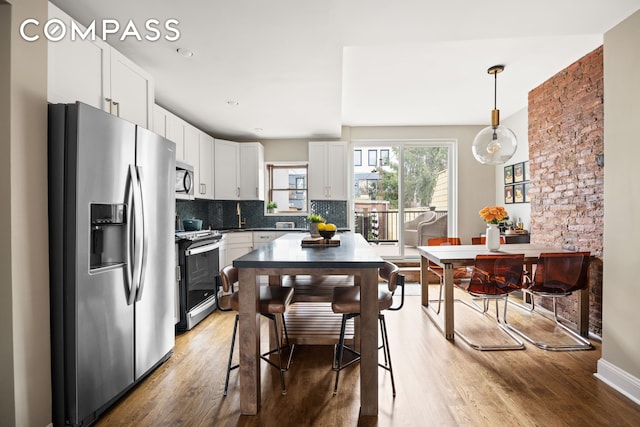 kitchen featuring light wood-type flooring, appliances with stainless steel finishes, white cabinets, decorative backsplash, and hanging light fixtures