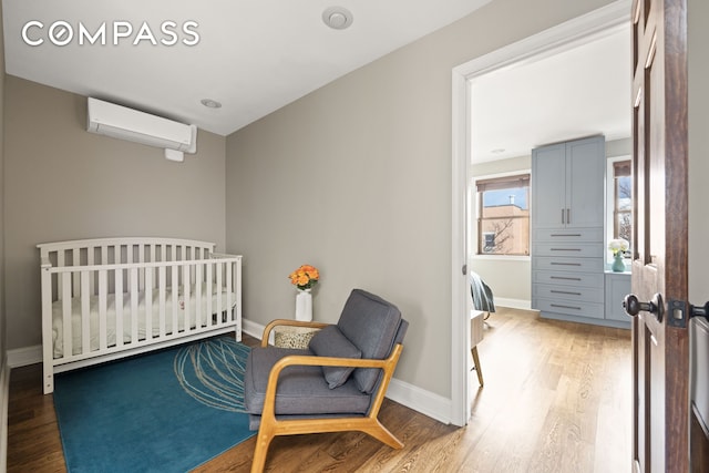 bedroom with an AC wall unit, a crib, wood finished floors, and baseboards