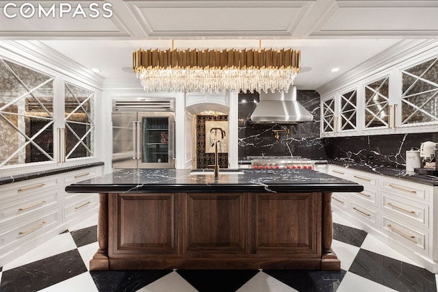 kitchen with wall chimney exhaust hood, stainless steel appliances, a center island with sink, decorative backsplash, and dark brown cabinetry