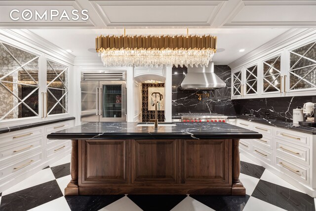 kitchen with wall chimney range hood, sink, appliances with stainless steel finishes, dark brown cabinetry, and a center island with sink