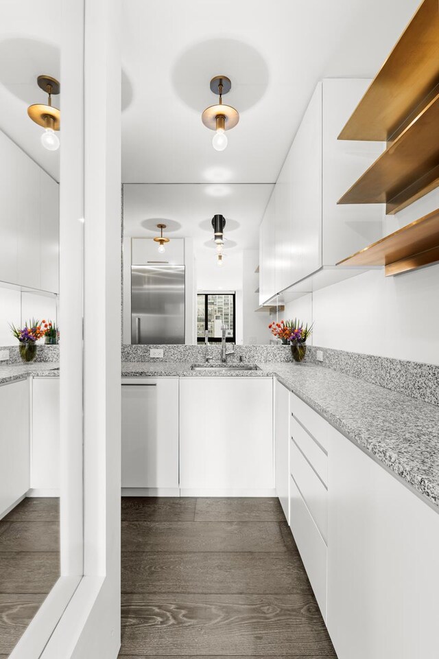 kitchen featuring light stone countertops, black appliances, dark wood-type flooring, white cabinetry, and sink