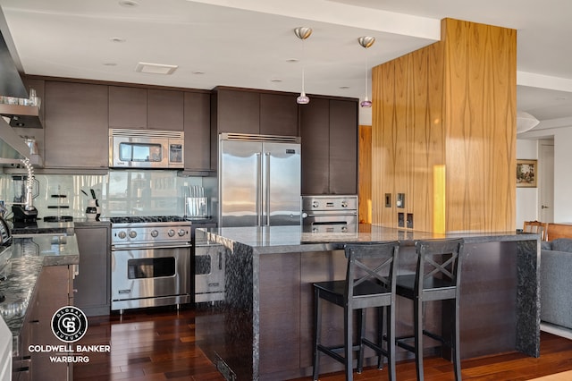 kitchen with backsplash, high quality appliances, a kitchen bar, dark stone countertops, and dark wood-style floors