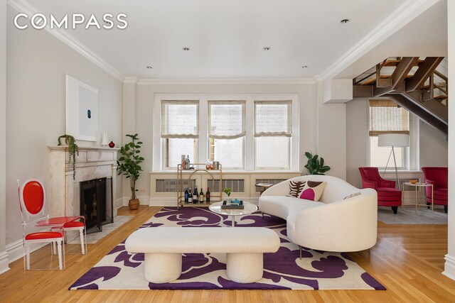 living room with crown molding, a high end fireplace, and light wood-type flooring